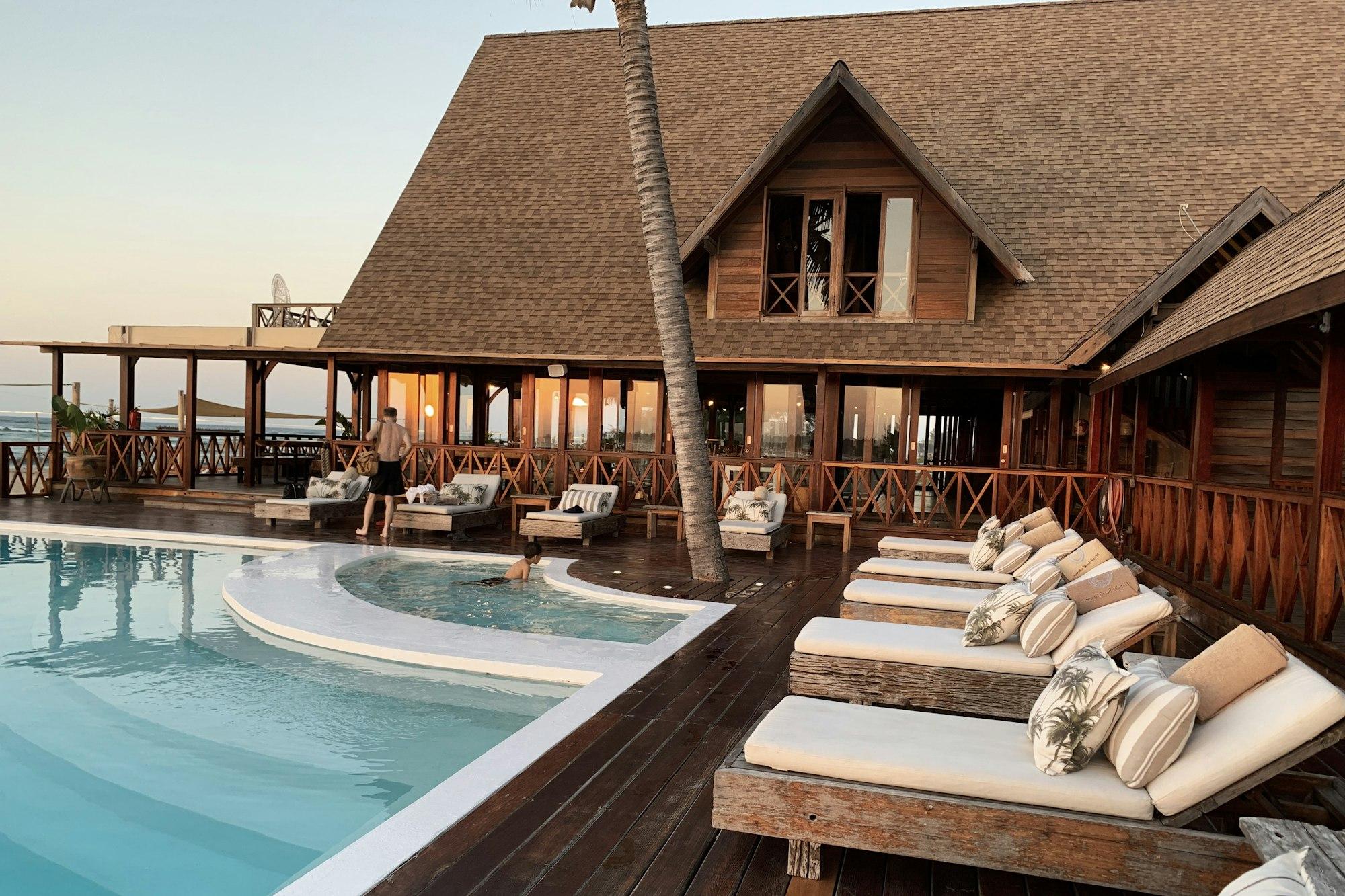 A wooden resort lodge with a thatched roof beside a swimming pool