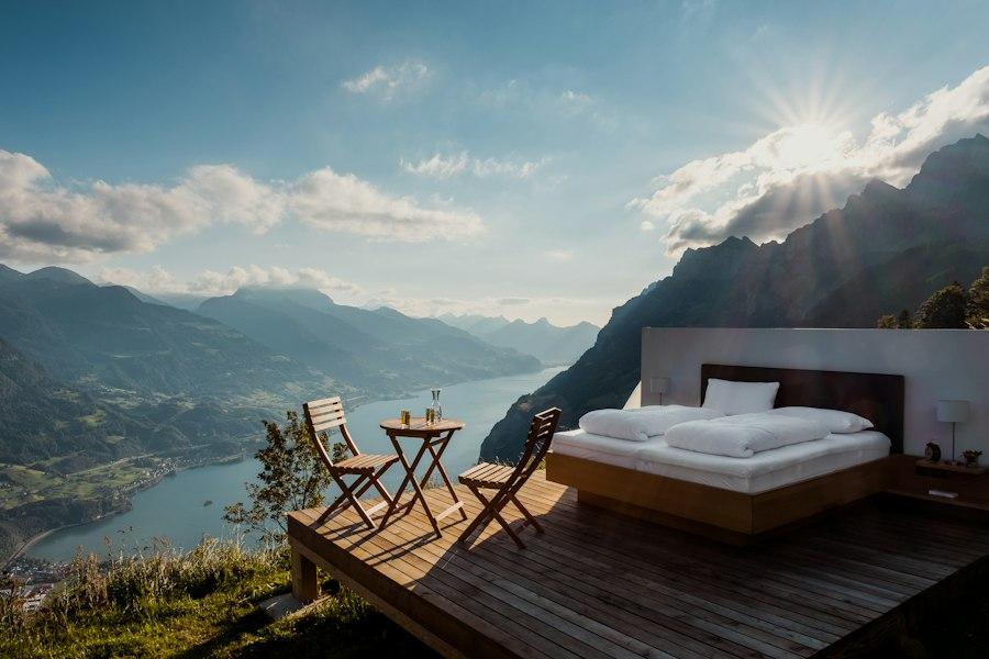 An outdoor bed on a wooden deck above a mountain lake